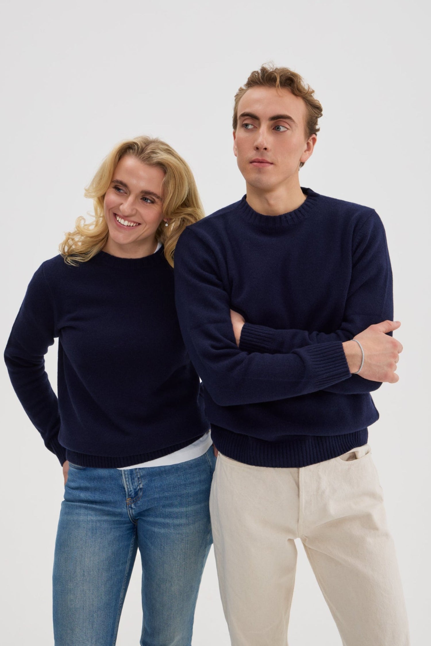 Two people wearing navy blue sweaters and jeans against a white background